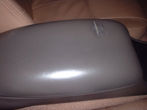 Close-up of a gray vinyl center console armrest lid with tan leather seats behind
