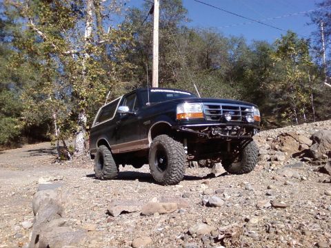 1995 Ford Bronco - Modified 1995 Ford Bronco tackling a rough, rocky terrain on a sunny day.