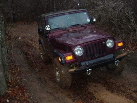 1995 Ford Bronco - A maroon Jeep Wrangler navigates a muddy off-road trail in overcast conditions.