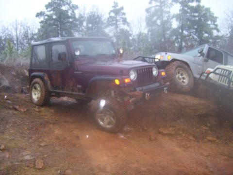 1995 Ford Bronco - Multiple off-road vehicles navigate a muddy terrain in a wooded area.