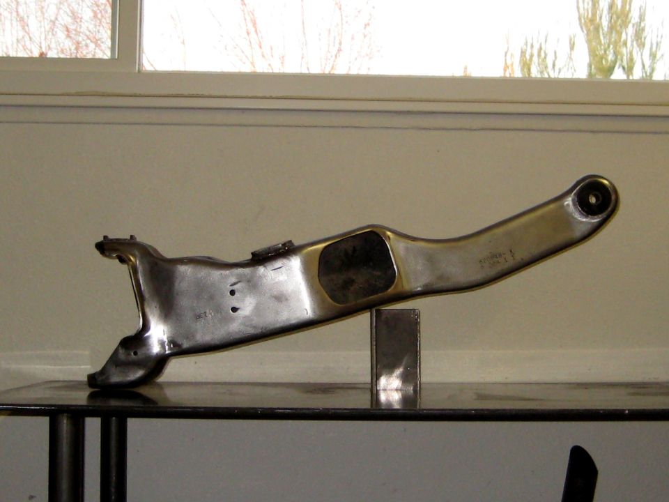 Shiny metal control arm with some stamped numbers on it, resting on a table