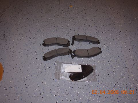 1995 Ford Taurus - A set of four brake pads are displayed on a garage floor, with two additional pads in a clear plastic bag.