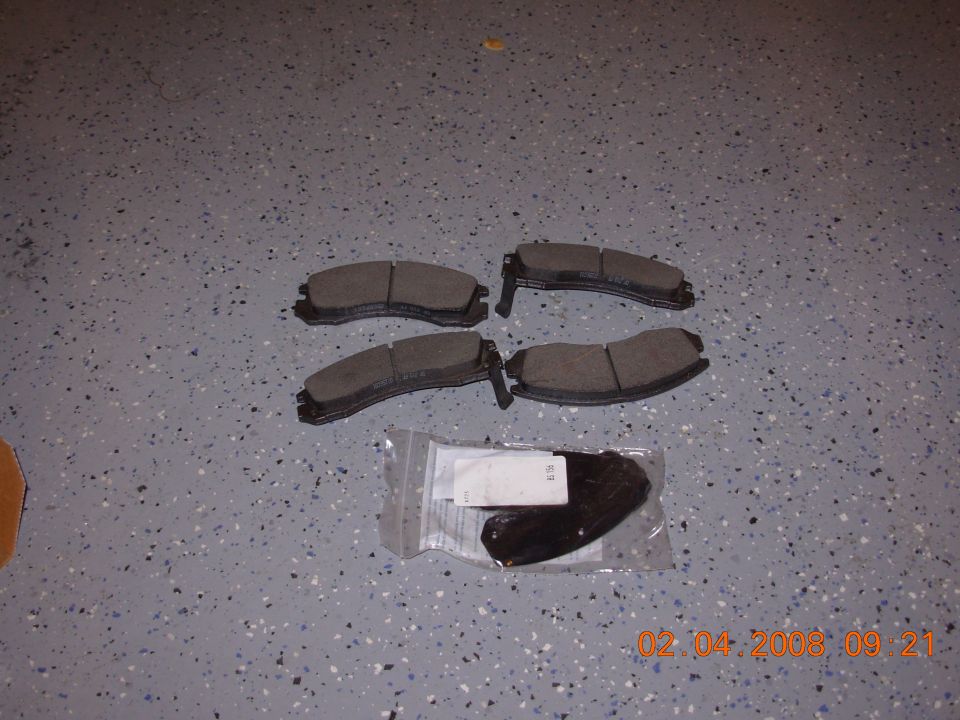 four brake pads laid out on a speckled floor, with two more in a plastic bag