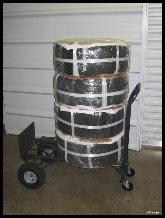 Stack of four tires wrapped in plastic on a dolly