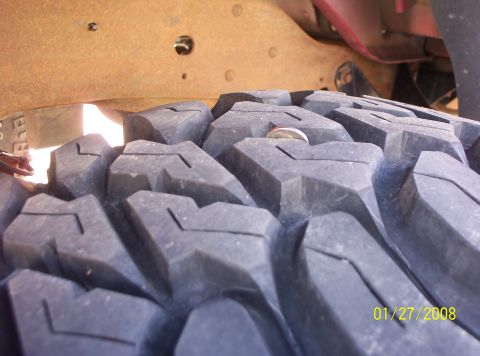 1995 Ford Bronco - A coin is stuck in the aggressive tread pattern of a vehicle's tire, with a rusty frame overhead.