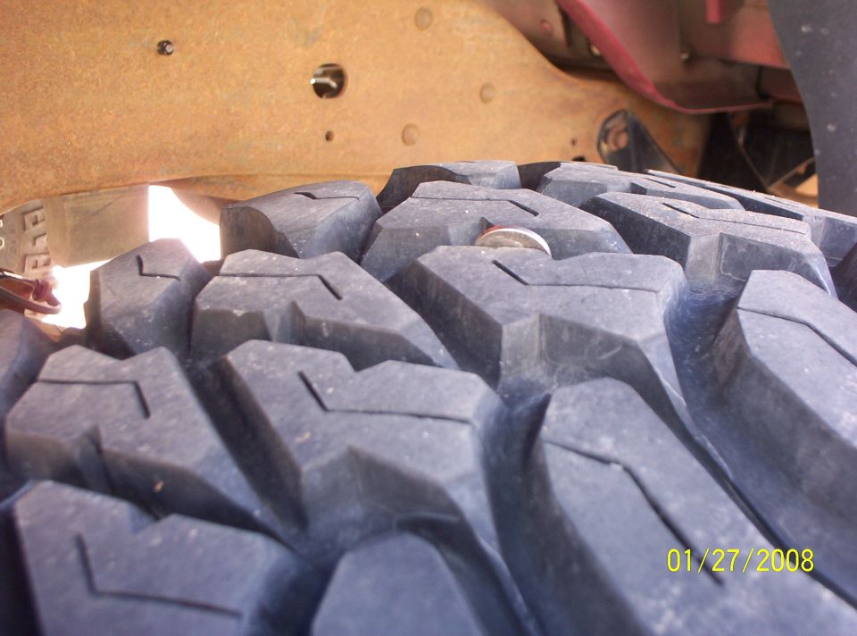 Close-up of a large, knobby tire tread with a coin lodged in it. Rusty frame visible above