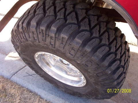 1995 Ford Bronco - A close-up view of a off-road tire and its polished rim, with a hint of red paint from the vehicle.
