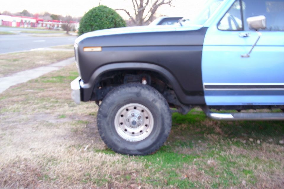 Front fender and wheel of a lifted blue and gray 1980s Ford truck on grass