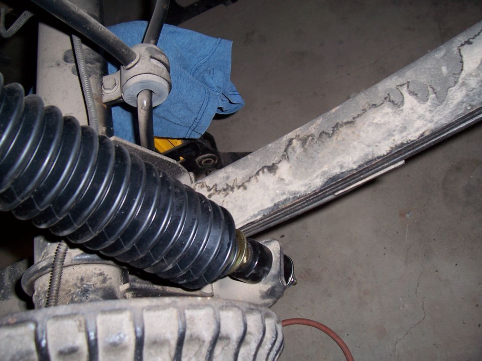close-up of a black rubber bellows on a steering component, with a leaf spring and part of a tire visible