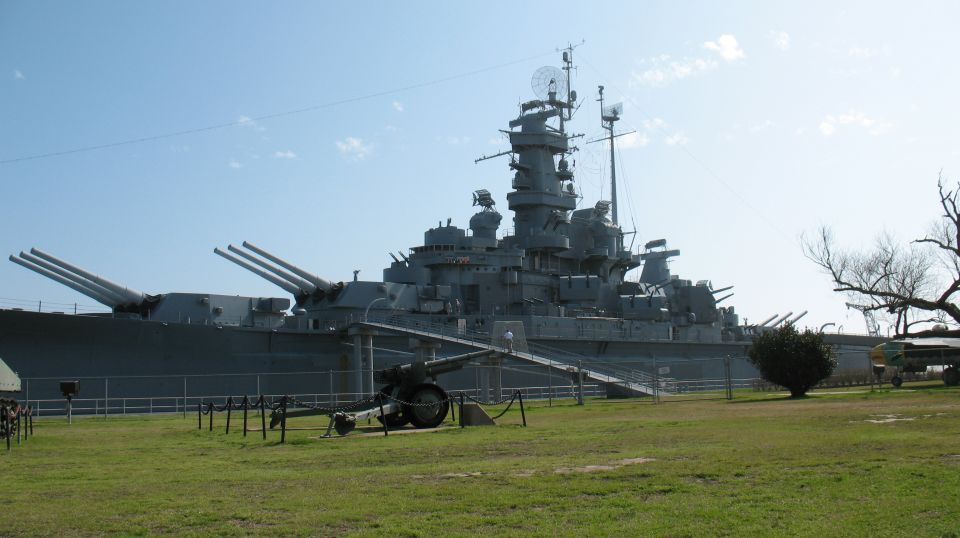 Battleship USS North Carolina with a cannon in the foreground, grassy field, and blue sky