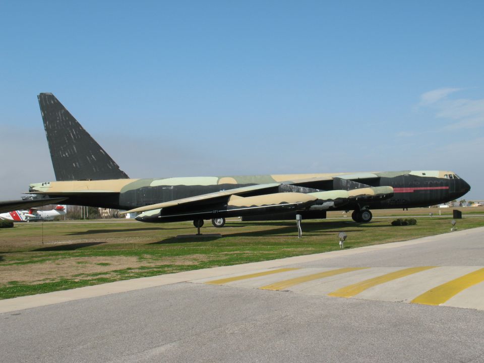 Bomber airplane with camouflage paint scheme on tarmac, another smaller aircraft visible in background