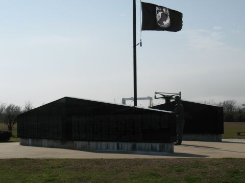 1997 Ford Crown Victoria - A solemn memorial site features a POW/MIA flag and black walls inscribed with names, set against a hazy sky.