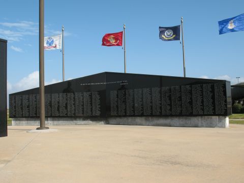 1997 Ford Crown Victoria - A war memorial wall stands under a clear blue sky, adorned with multiple flags representing different branches of service.