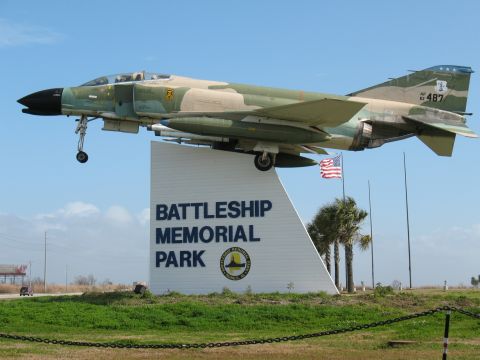 1997 Ford Crown Victoria - A fighter jet is displayed at Battleship Memorial Park with an American flag flying nearby.