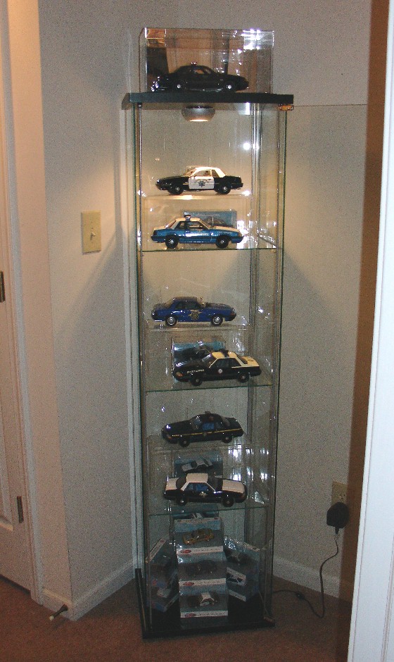 Glass display case filled with die-cast model police car collectibles on lit shelves