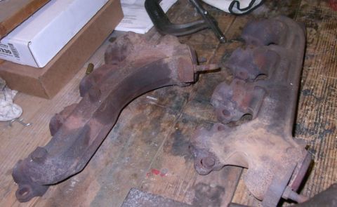 1994 Ford Bronco - Two rusty exhaust manifolds are shown on a wooden surface, possibly for a Ford Bronco.
