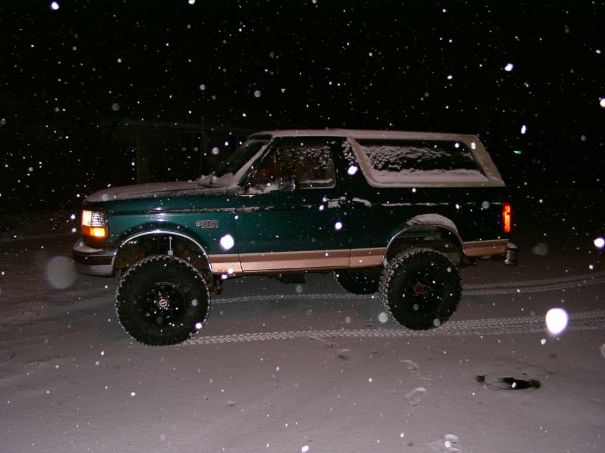 Green Ford Bronco with tan trim parked outside in falling snow