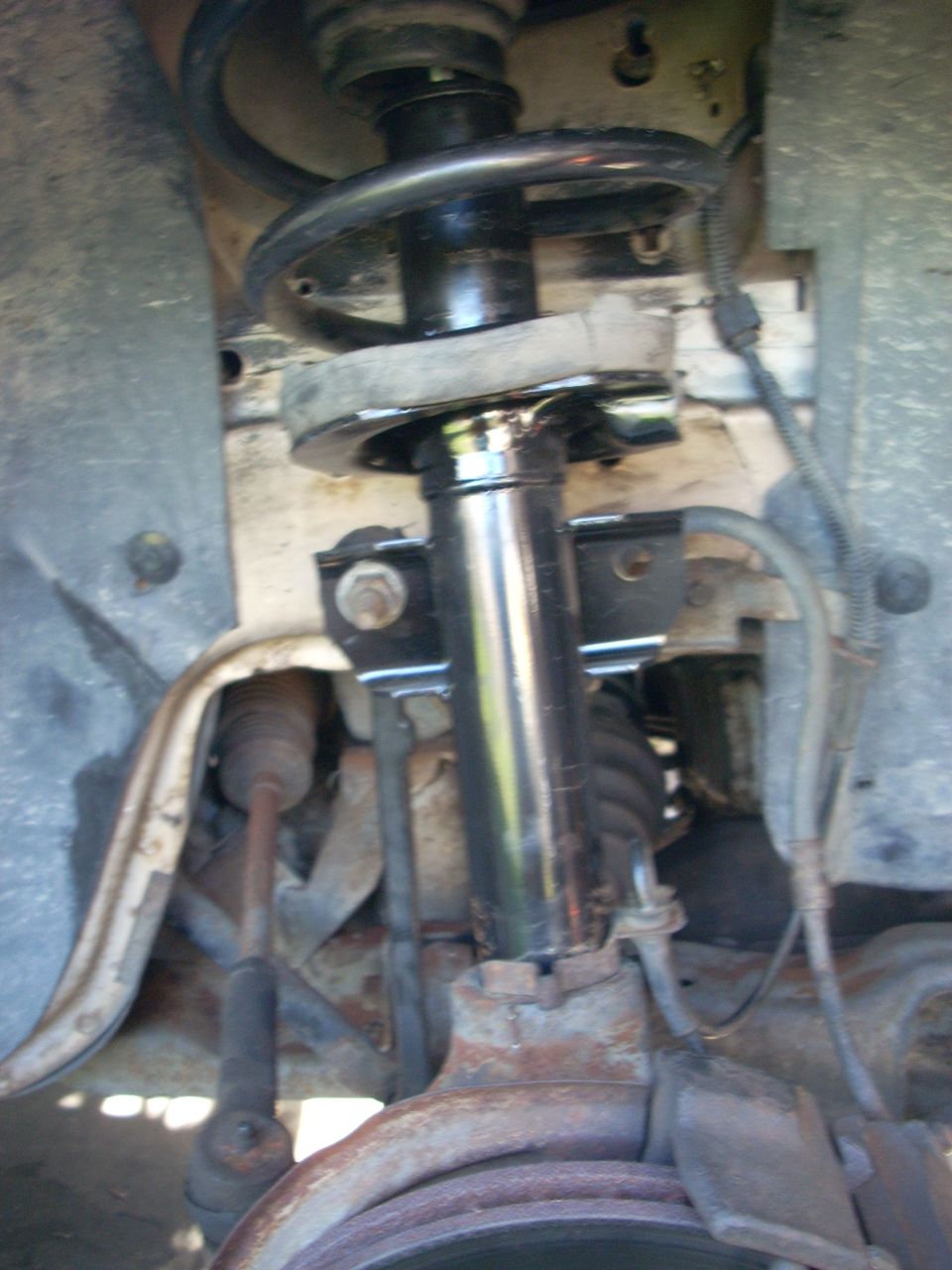 Front suspension strut assembly with black coil spring and rusty metal components