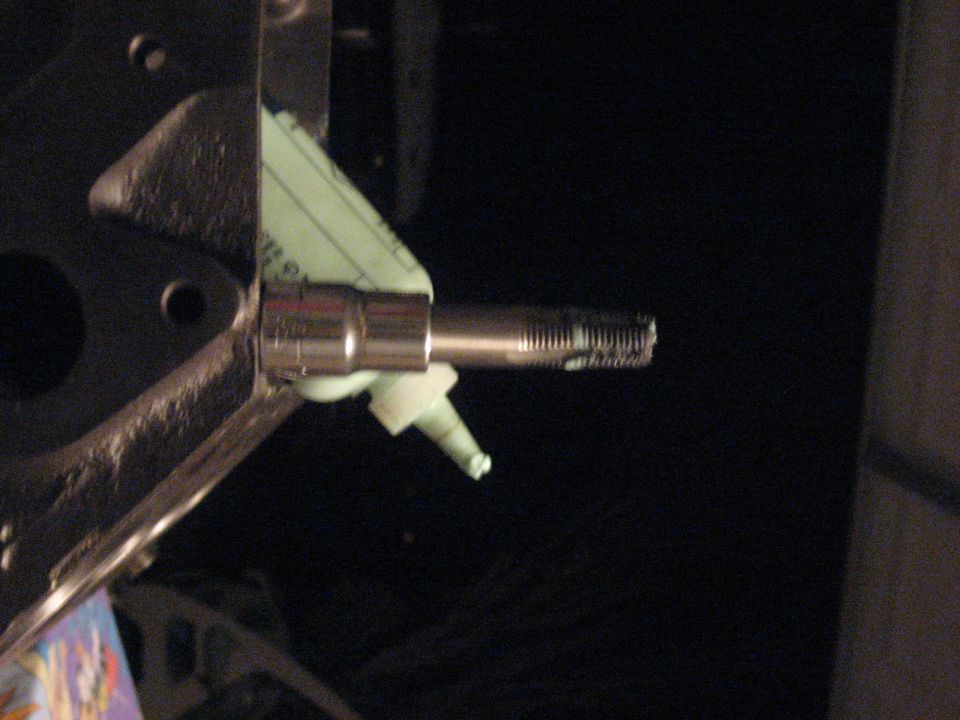 Long threaded stud in chrome socket held by a tool beside a mint-green plastic part in a dark engine bay