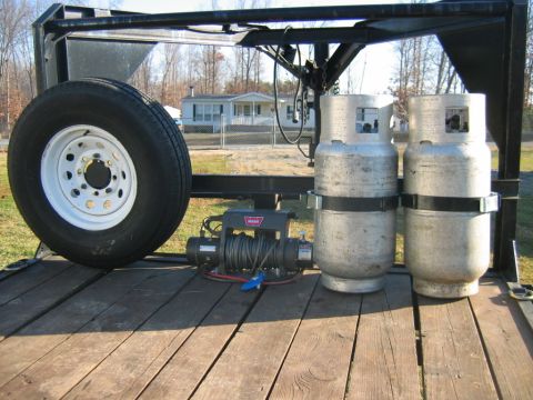 1992 Ford Mustang - A trailer bed holds a spare tire, a winch, and two propane tanks, with a house visible in the distance.