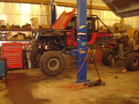 1992 Ford Bronco - A red Jeep Wrangler is undergoing repairs in a workshop, elevated on a hydraulic lift.