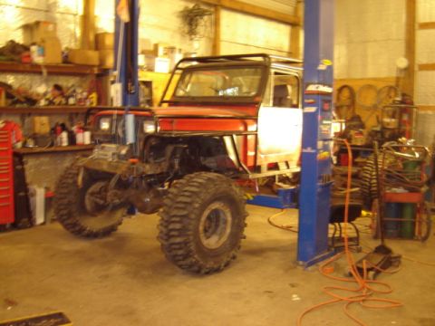 1992 Ford Bronco - Modified Jeep CJ-7 on a lift in a workshop, showing its off-road tires and roll cage.