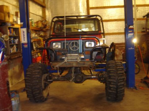 1992 Ford Bronco - This heavily modified Jeep Wrangler is on a lift inside a garage, showing its large tires and front winch.