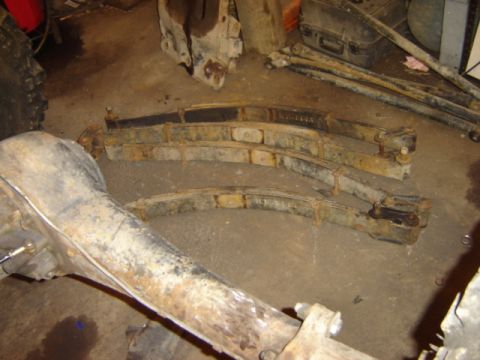 1992 Ford Bronco - Close-up of vehicle suspension components, including leaf springs and a rear axle, lying on a workshop floor.