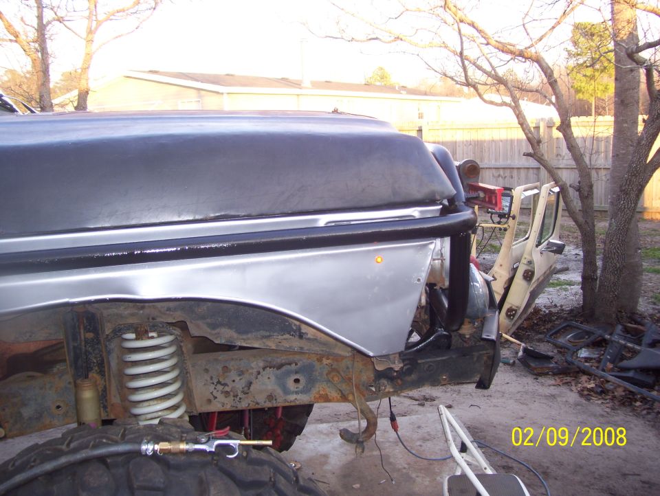 Silver fender and open door of a vehicle, with visible suspension and tire