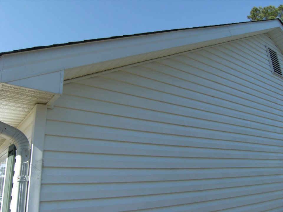 Gable end of a cream vinyl-sided house with gable vent against blue sky