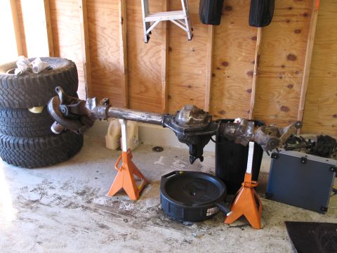 1995 Ford Bronco - A front axle assembly is supported by jack stands in a garage, with stacked tires to the left.