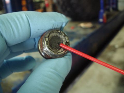 1996 Ford Bronco - A gloved hand holds a differential fluid drain plug covered in debris, with a red nozzle inserted into it.