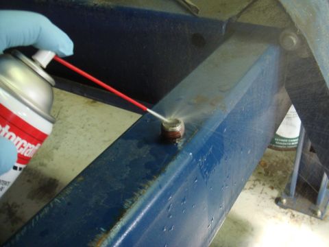 1996 Ford Bronco - A bolt is sprayed with lubricant from a can held by a gloved hand.