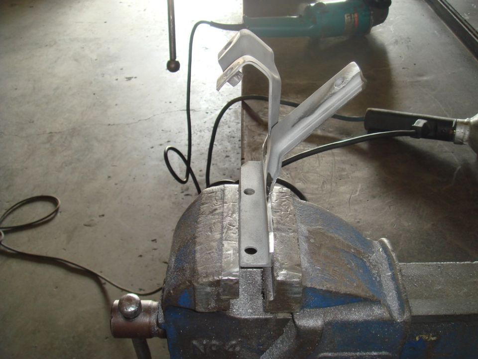 Metal bracket clamped in a vise, with power tools in the background
