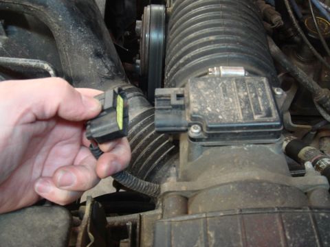 1996 Ford Bronco - Close-up of a hand disconnecting an electrical connector from a vehicle's air intake sensor assembly.