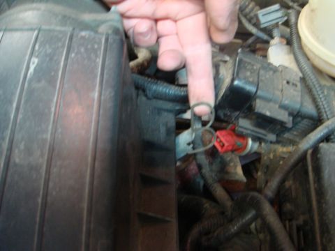 1996 Ford Bronco - A hand points to a metal clip in a cluttered engine bay, with various hoses and electrical components visible.