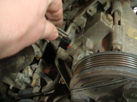 1996 Ford Bronco - A hand disconnects a wire harness from a component within the engine bay.