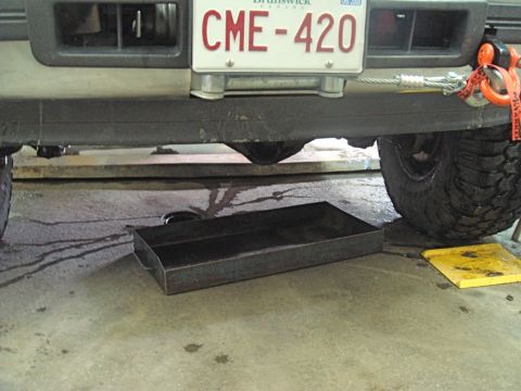 1996 Ford Bronco - A drain pan is positioned under the rear axle of a vehicle, catching drips.