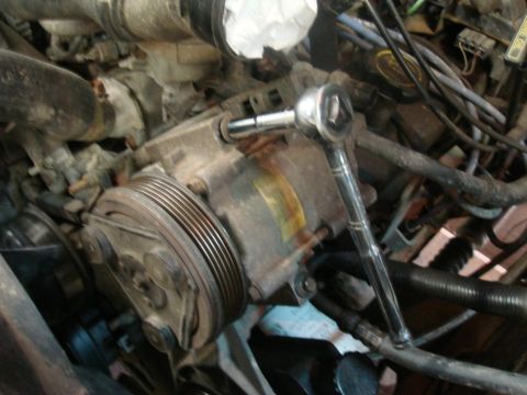 1996 Ford Bronco - A socket wrench is used on a dirty engine part in this close-up view.