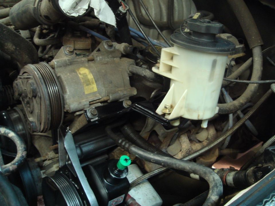 Engine bay with power steering pump, AC compressor, and fluid reservoir