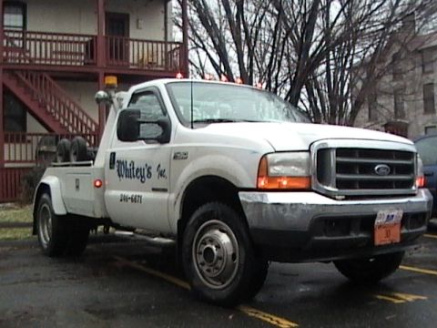 1990 Ford Bronco - A white tow truck with "Whitey's Inc." and a phone number is parked on a wet surface.
