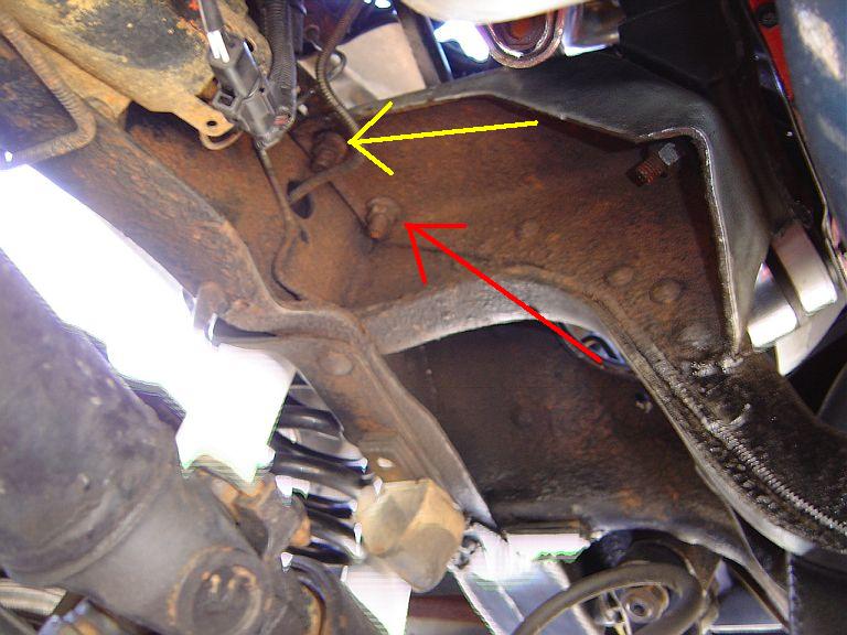 Close-up of rusty vehicle frame with yellow and red arrows pointing to components. Supermotors.net logo visible