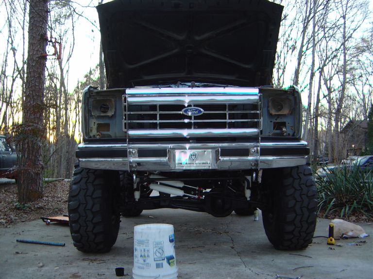 Front view of a lifted Ford truck with hood open, showing large tires and chrome grille