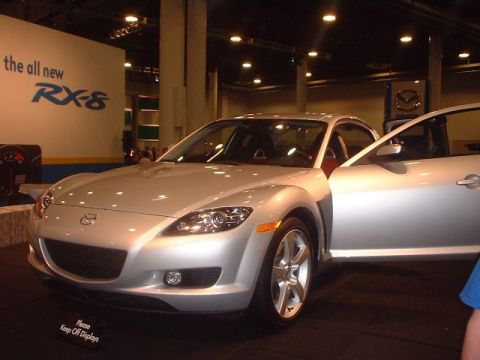 1996 Ford Taurus - Mazda RX-8 displayed at an auto show with "the all new RX-8" signage.