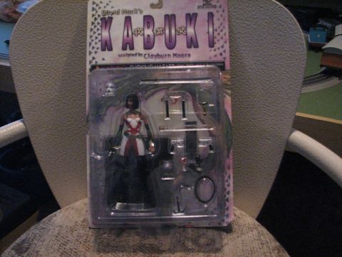 1991 Ford Bronco - A packaged Kabuki action figure, sculpted by Clayburn Moore, is displayed on a chair.