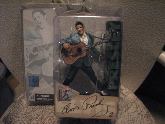 Elvis Presley action figure with guitar in plastic packaging, text reads 'Elvis Presley'