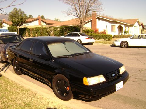 1991 Ford Taurus - A black 1991 Ford Taurus sedan is parked on the side of a residential street.