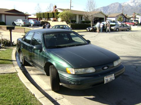 1991 Ford Taurus - Green 1991 Ford Taurus parked in a driveway with other vehicles in the background.
