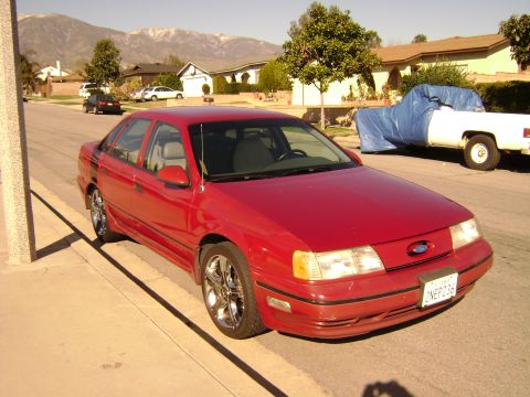 1991 Ford Taurus - Red 1991 Ford Taurus parked curbside in a suburban neighborhood with mountains in the distance.
