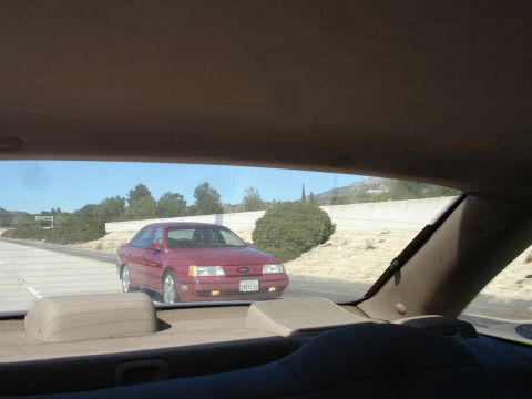 1991 Ford Taurus - A red 1991 Ford Taurus sedan is seen from the rear passenger seat while driving on a highway.